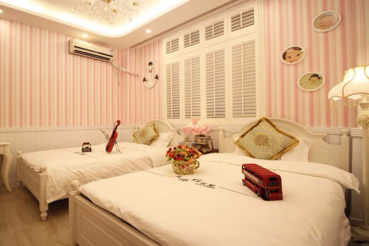 A room with two beds, a vanity with a mirror, a red bus toy, and striped wallpaper.