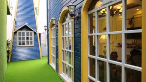 Un couloir étroit, avec un immeuble bleu d’un côté et un immeuble jaune de l’autre, tous deux dotés de grandes fenêtres et d’une pelouse artificielle verte.