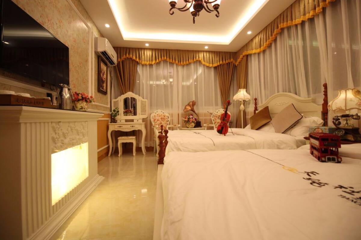 A hotel room with two beds, a TV, a fireplace, and a desk with a lamp.