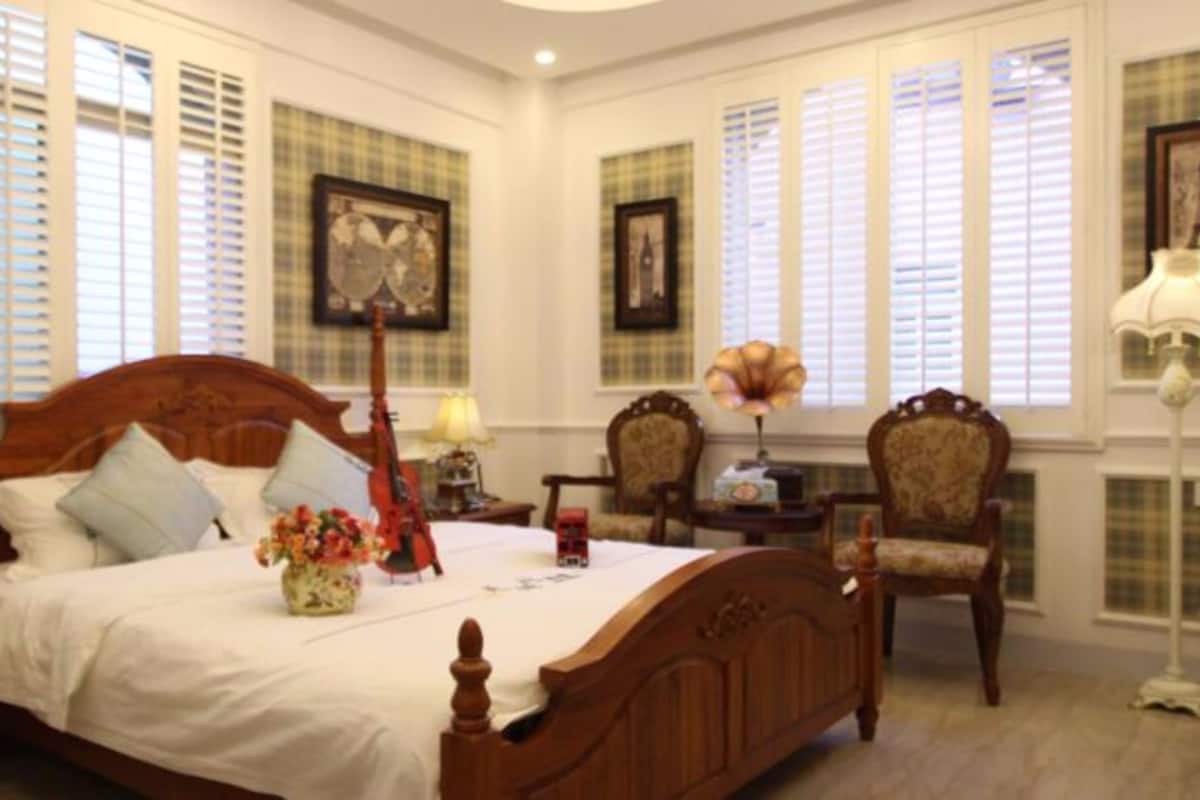 A bedroom with a large bed, two chairs, a desk, and a lamp.