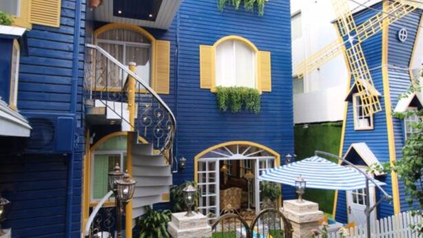 Un bâtiment à deux étages, avec une façade bleue, des bordures jaunes et une clôture blanche en piquets.