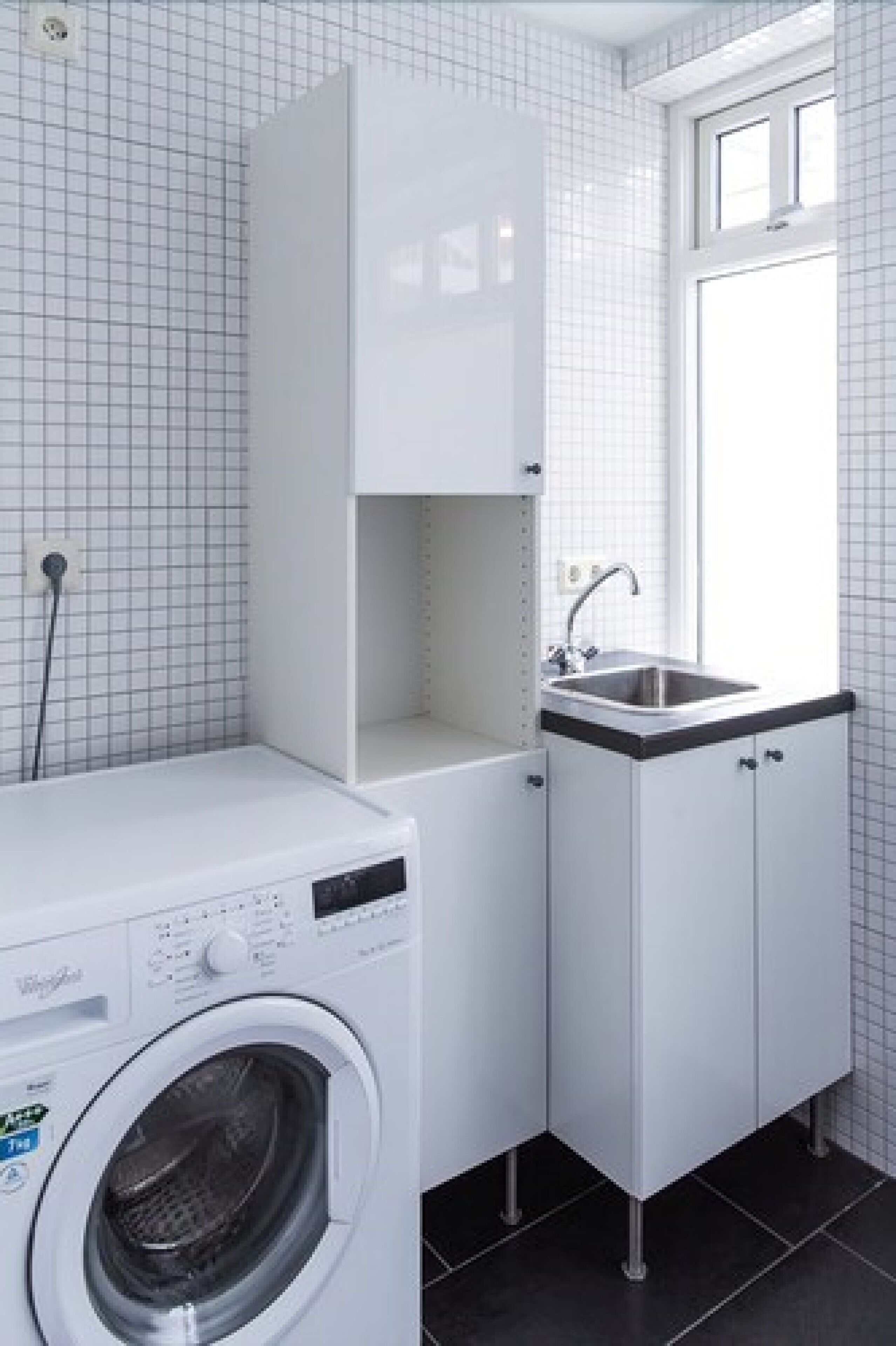 Un espacio pequeño para la lavandería con lavadora, lavamanos y un mueble.