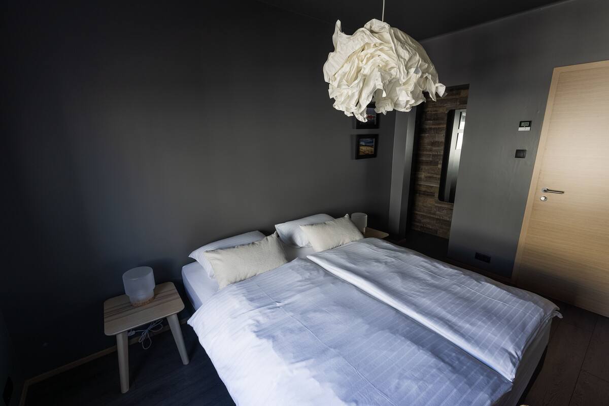 A bedroom with a bed, bedside table, and a hanging light fixture.