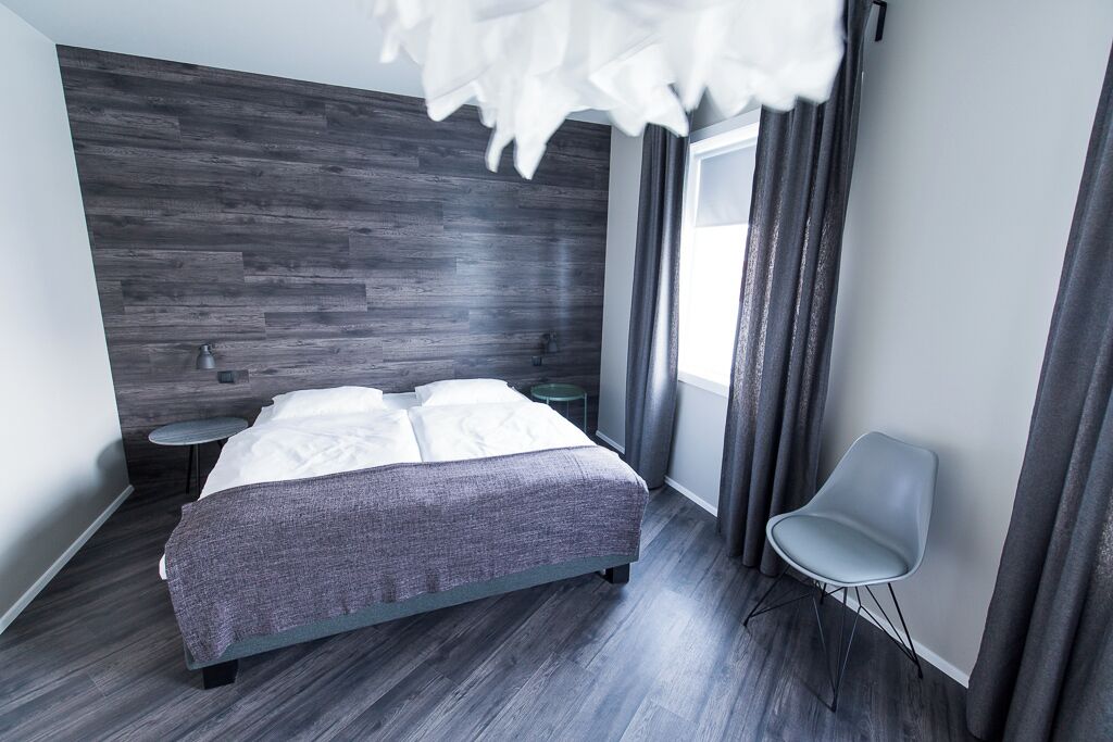 A modern bedroom with a bed, a chair, a nightstand, and a window with curtains.