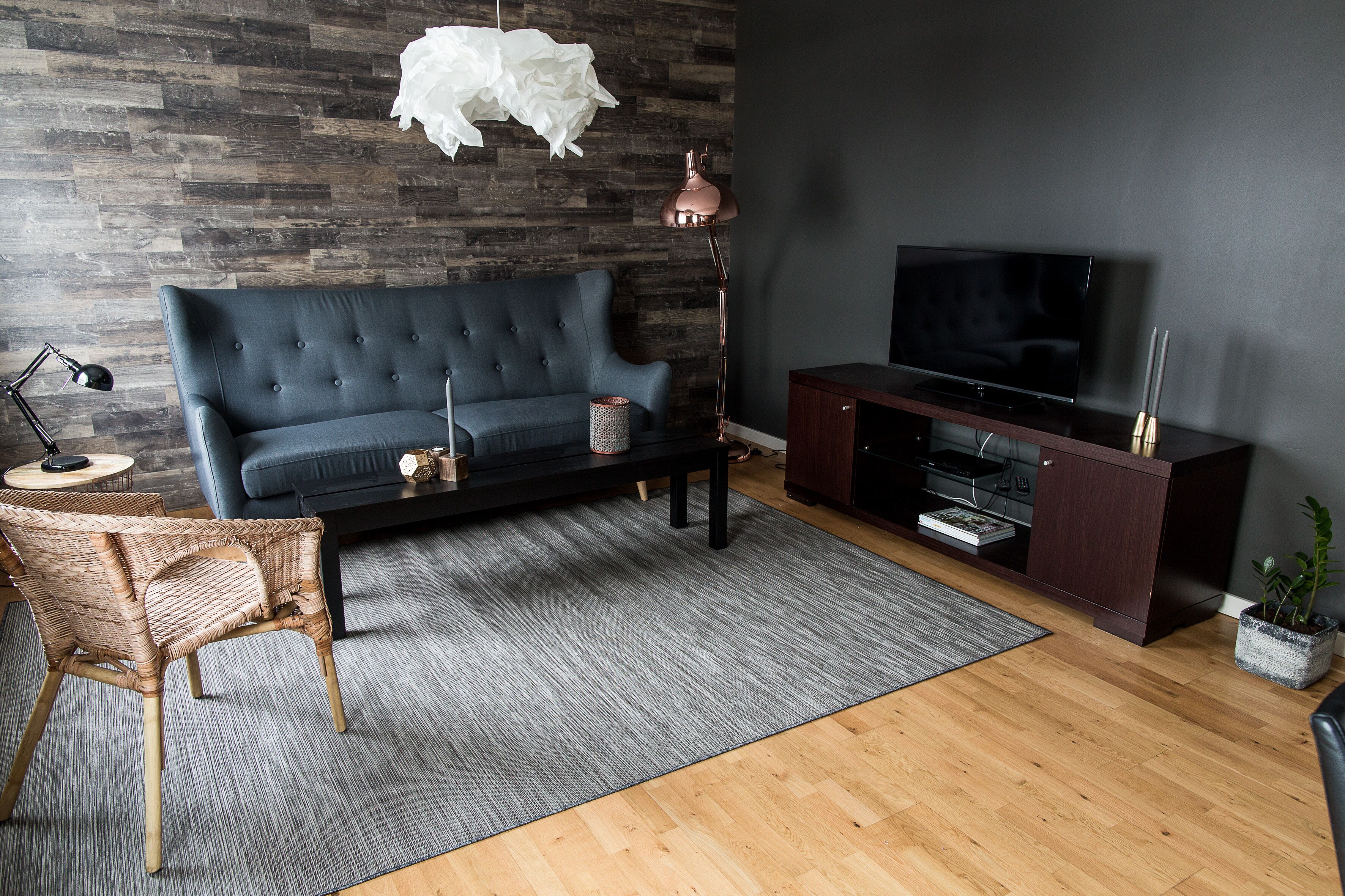 A modern living room with a dark blue sofa, a wooden coffee table, a black TV stand, and a wicker chair.