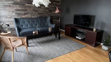 A modern living room with a dark blue sofa, a wooden coffee table, a black TV stand, and a wicker chair.