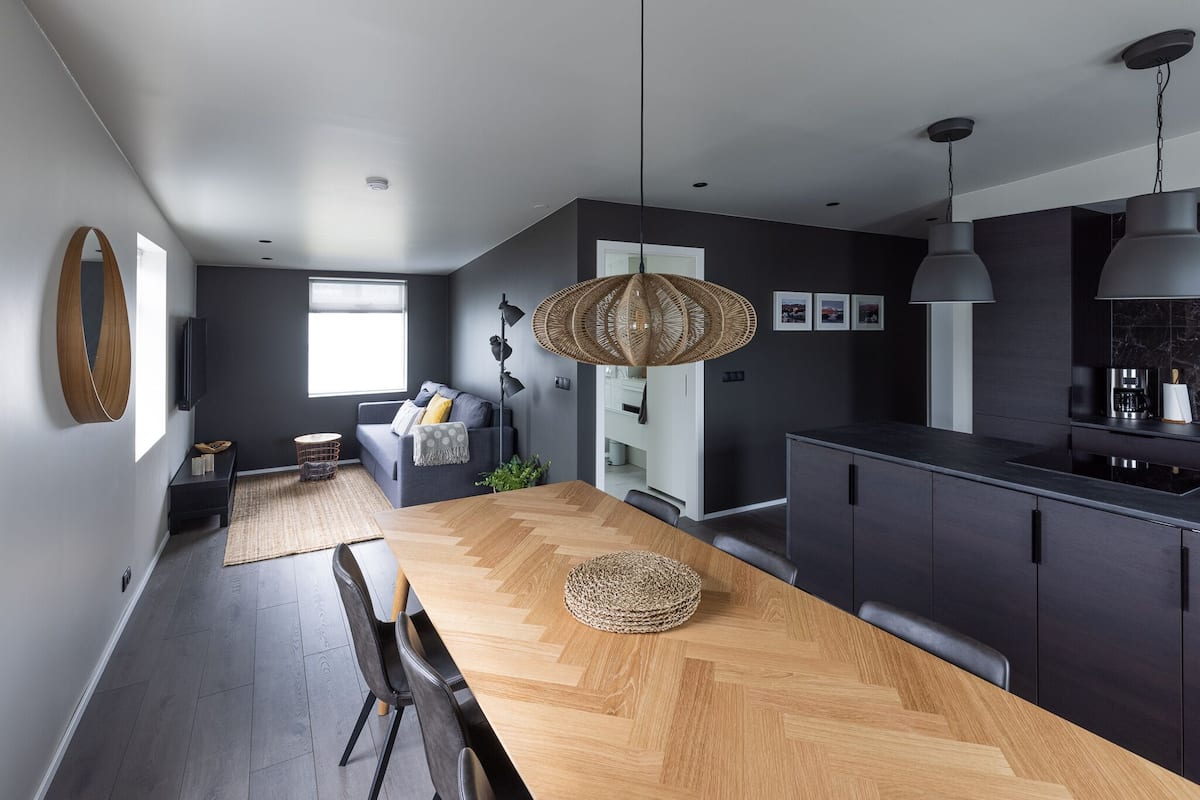 A modern kitchen with dark cabinetry, a wooden dining table, and pendant lighting.