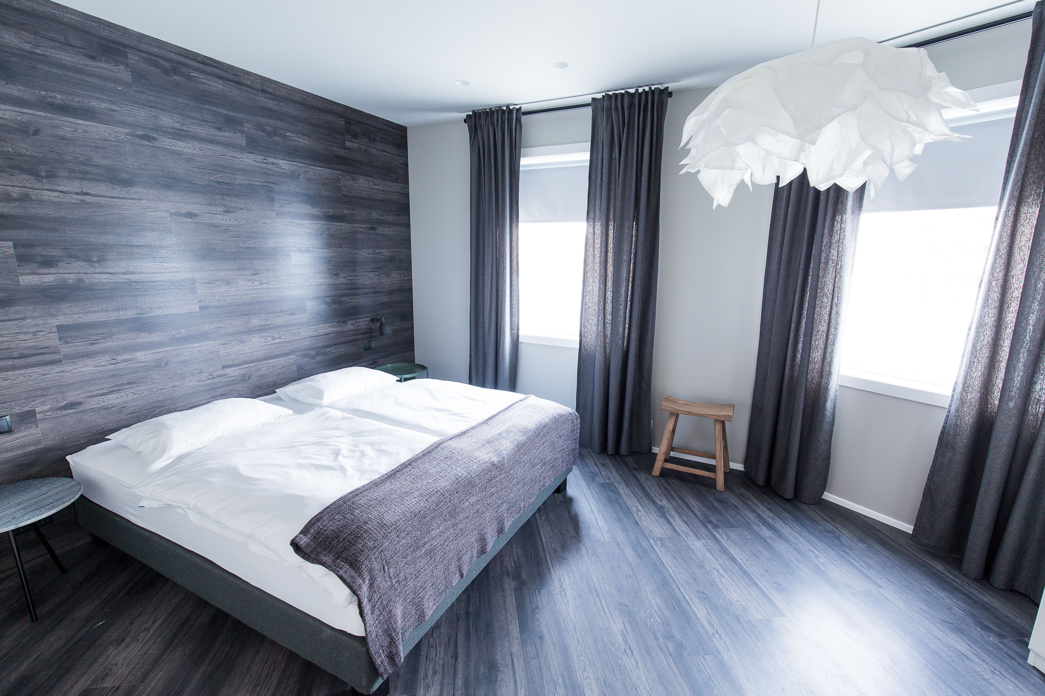 A modern bedroom with a large bed, dark wooden flooring, and a small stool.
