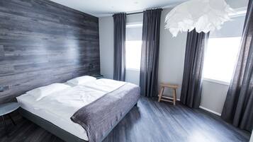 A modern bedroom with a large bed, dark wooden flooring, and a small stool.