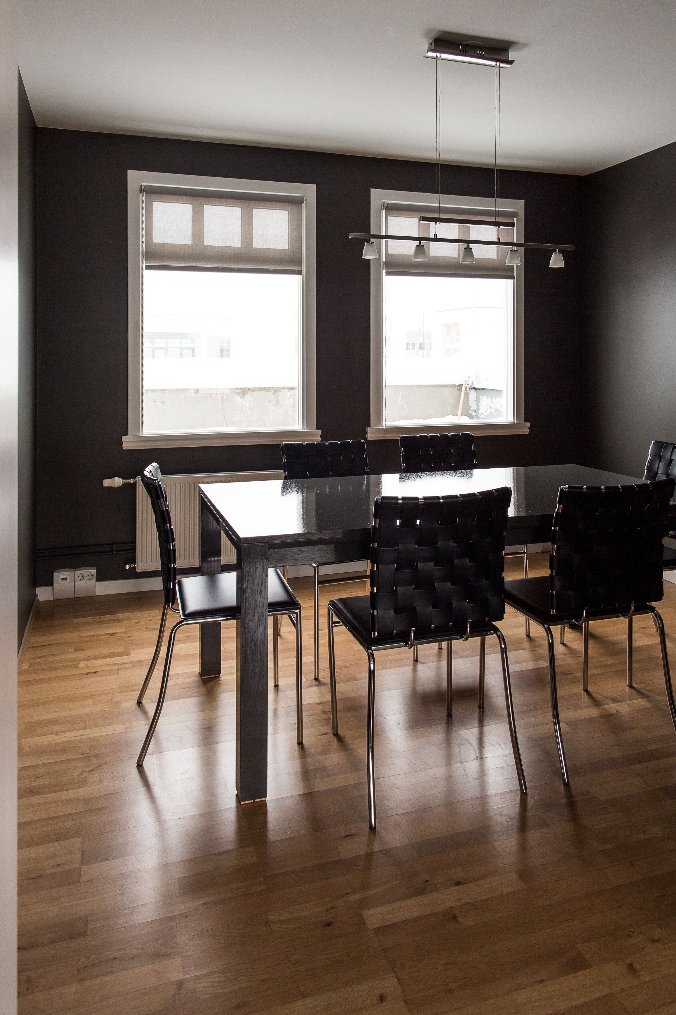 A modern dining area with a rectangular table, black upholstered chairs, and a hanging light fixture.