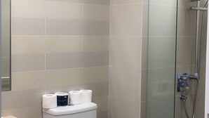 Ein Badezimmer mit Toilette, einer Duschkabine aus Glas und beigen Fliesen.