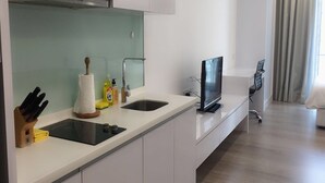 Eine moderne Küche mit weißen Schränken, einer schwarzen Arbeitsplatte, einem eingebauten Herd und einem Flachbildfernseher.