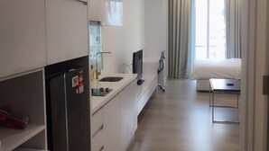 Ein modernes Hotelzimmer mit Küchenzeile, einem Bett, einem Fernseher und einem Fenster mit Vorhängen.