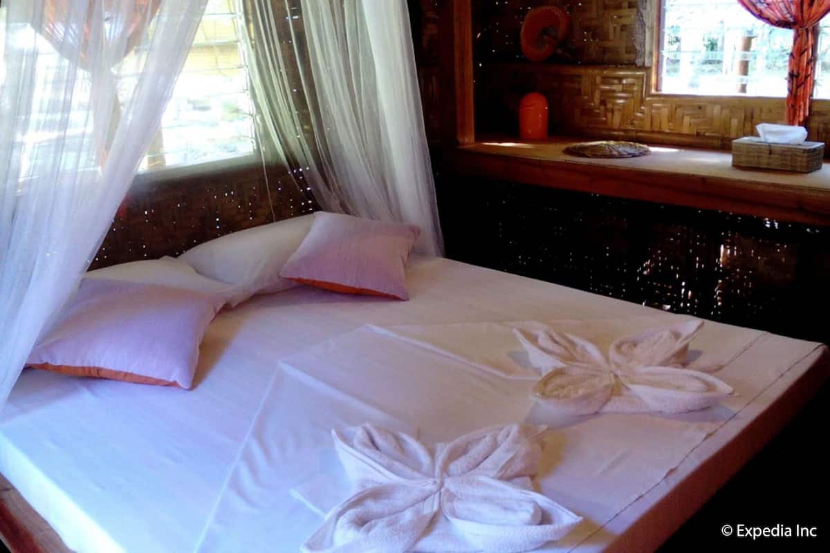A bed with white linens and a canopy, a wooden headboard, and a window with a view of the outdoors.