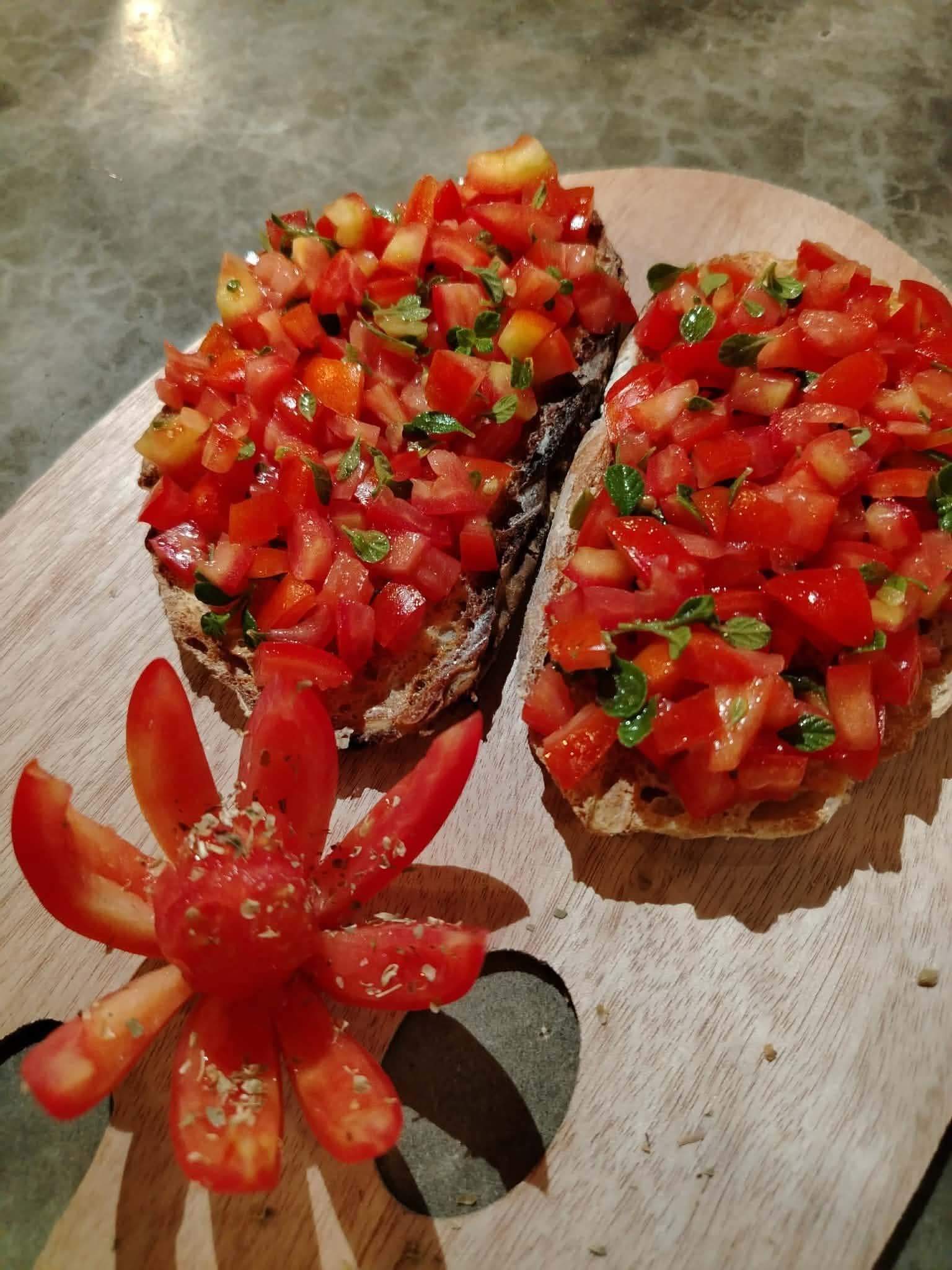 Two slices of toast topped with diced tomatoes and herbs on a wooden cutting board.