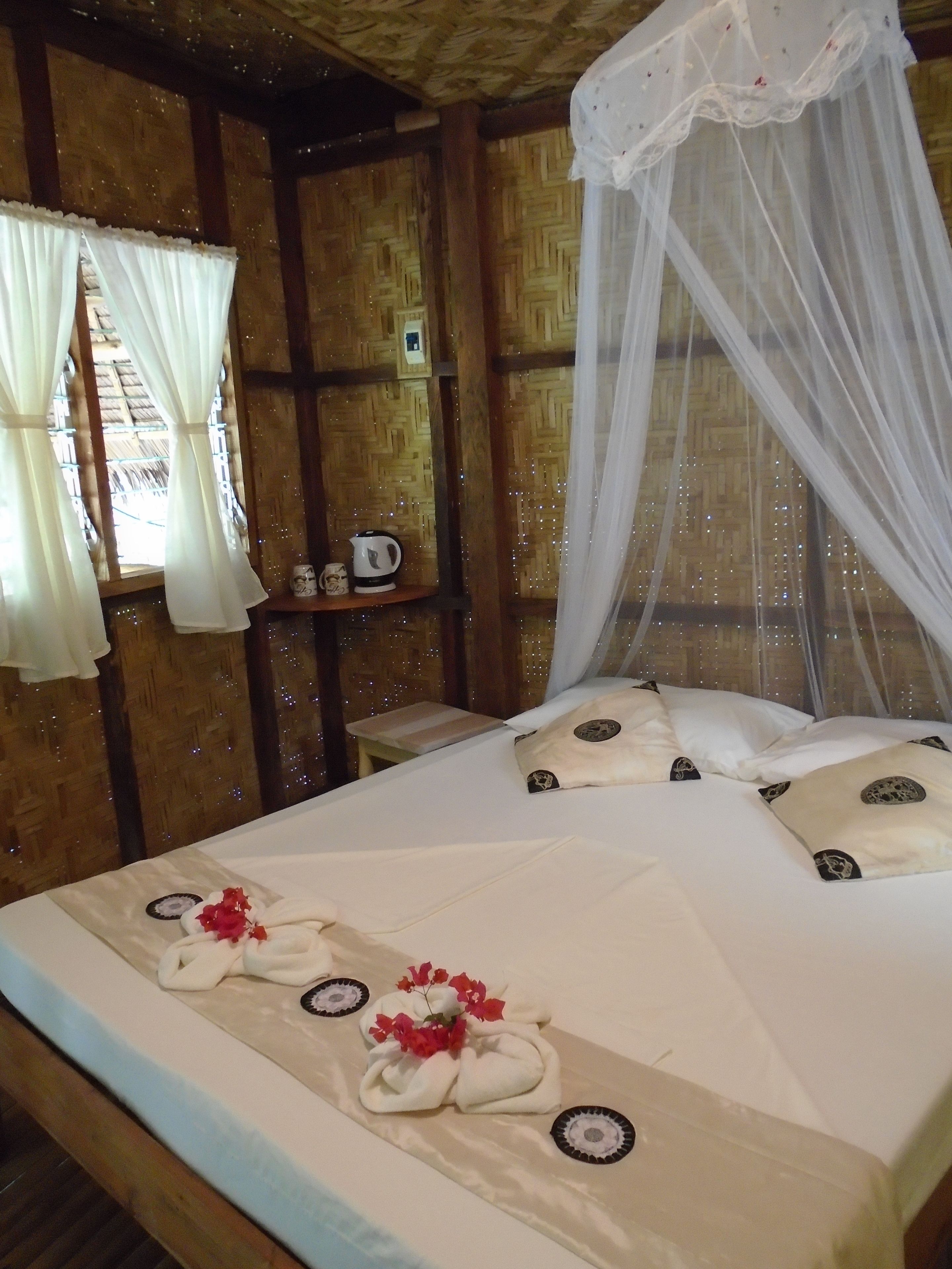 Una cama con sábanas blancas, dosel y almohadas decorativas.