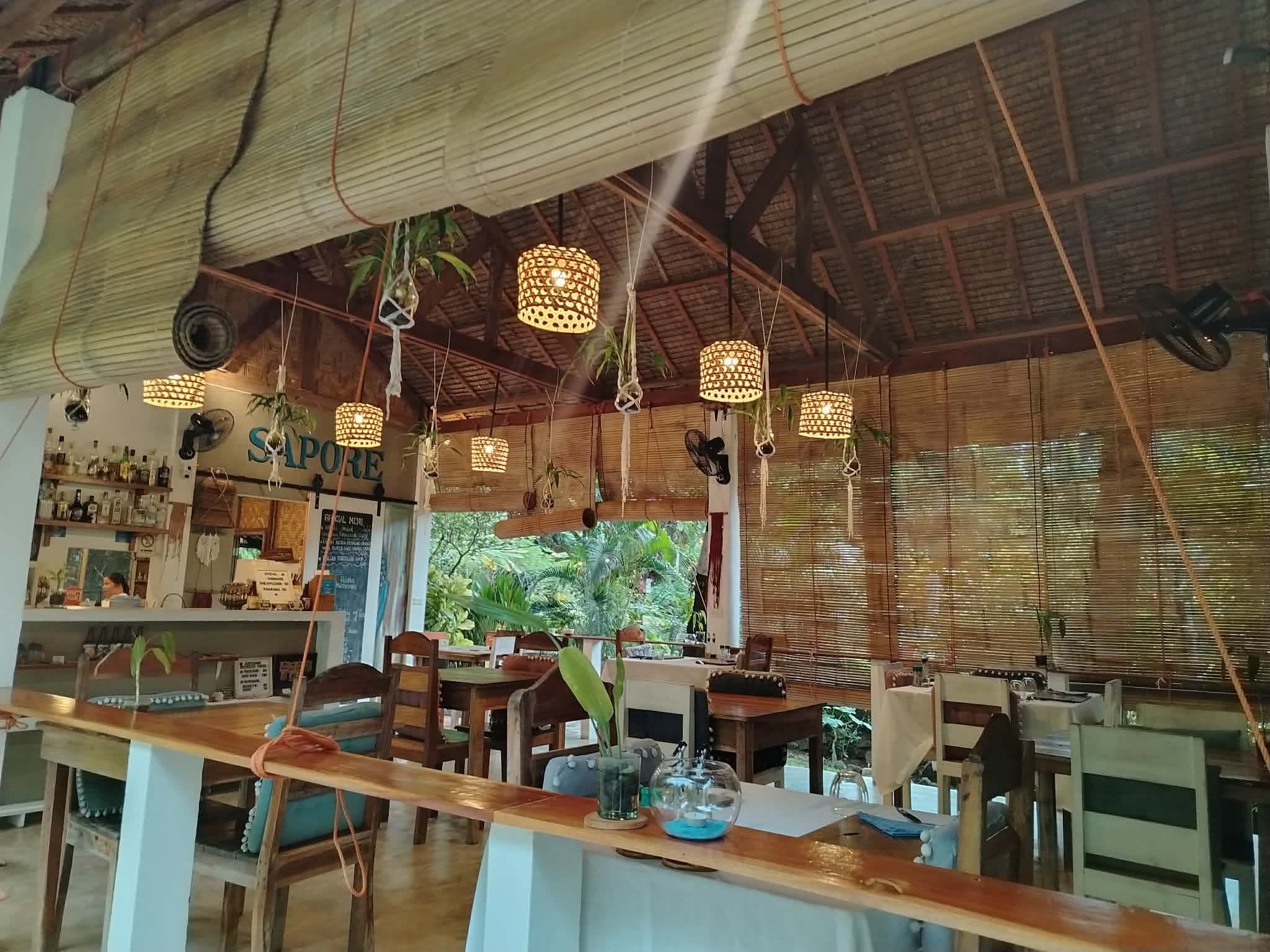 A restaurant with a rustic interior, featuring hanging lights, wooden furniture, and a visible menu board.
