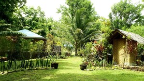 A lush garden with a thatched-roof structure, a paved pathway, and a sign indicating a restaurant. - Nypa Style Resort Camiguin (Mambajao)