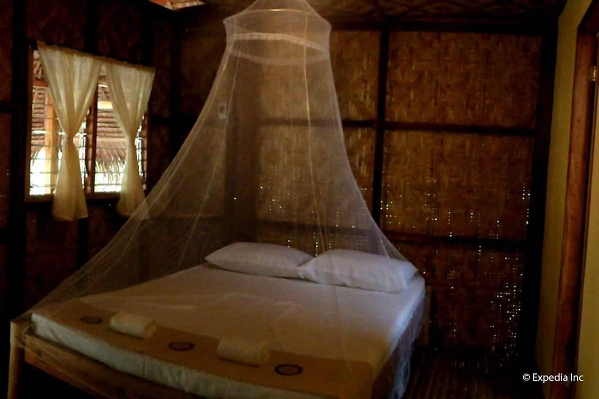 A room with a bed under a mosquito net, wooden walls, and a window with curtains.