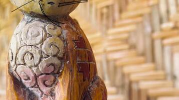 Una escultura de madera de un gato con cuerpo texturizado y cara plana, sobre un pedestal de madera.