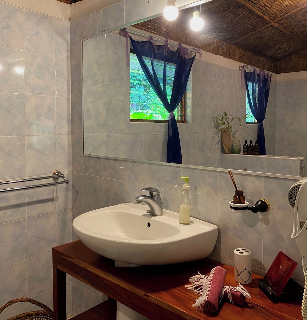 A bathroom with a large mirror, a white sink, a towel, a bottle of soap, and a fan.