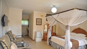 Quarto de hotel com cama, área de estar com cadeiras, pequeno frigorífico, televisão e ventoinha no teto.