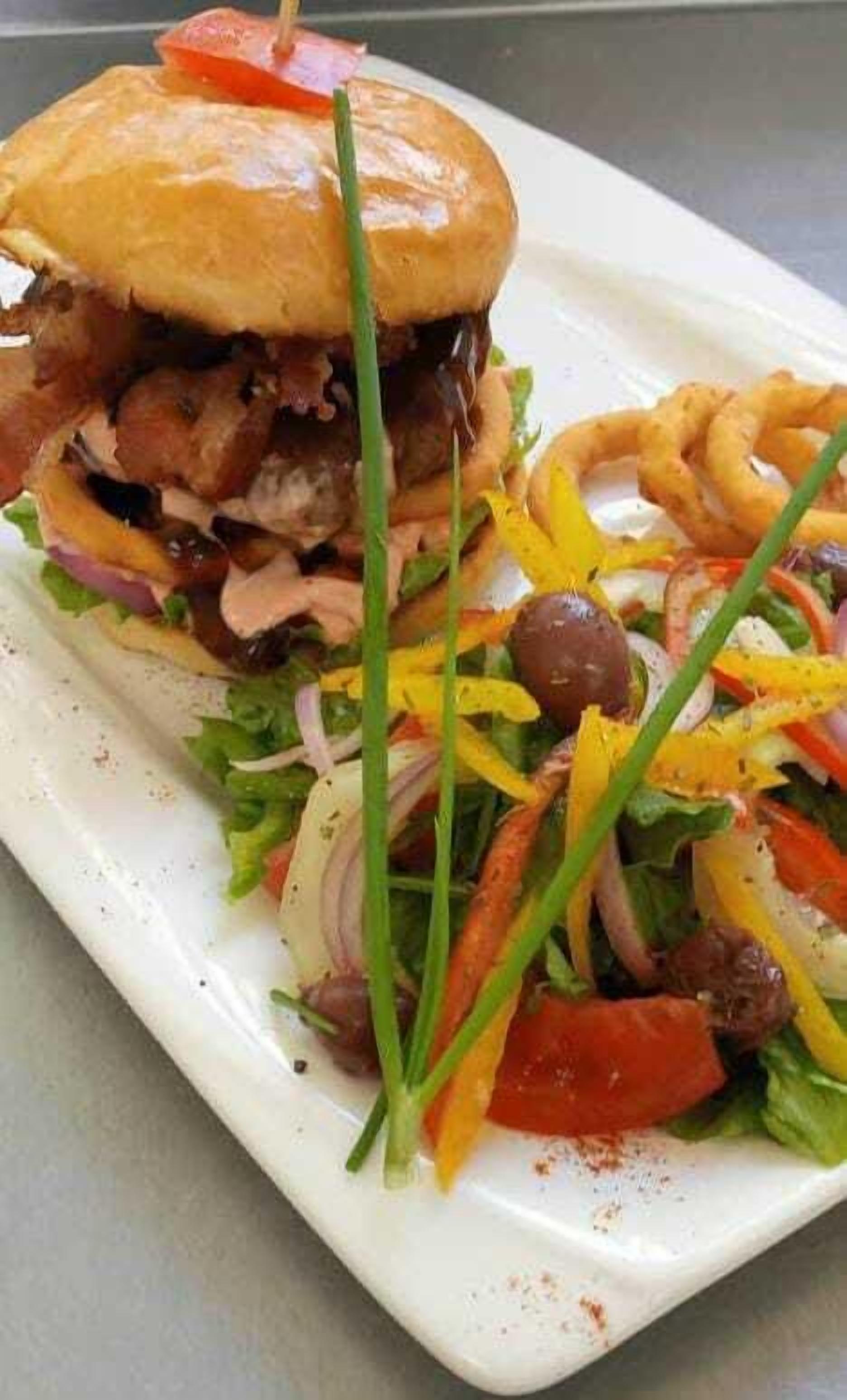 A sandwich with lettuce, tomato, and possibly meat, alongside a salad with mixed vegetables and a side of onion rings.