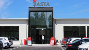 A building with a sign reading "RASTA" and a parking lot with several cars.