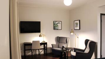 Una habitación con escritorio, dos sillas, televisor y cuadros en la pared.