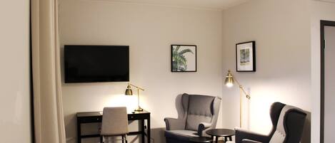 Una habitación con escritorio, dos sillas, televisor y cuadros en la pared.