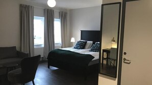 A hotel room with a bed, a chair, a table, a lamp, and a large mirror.