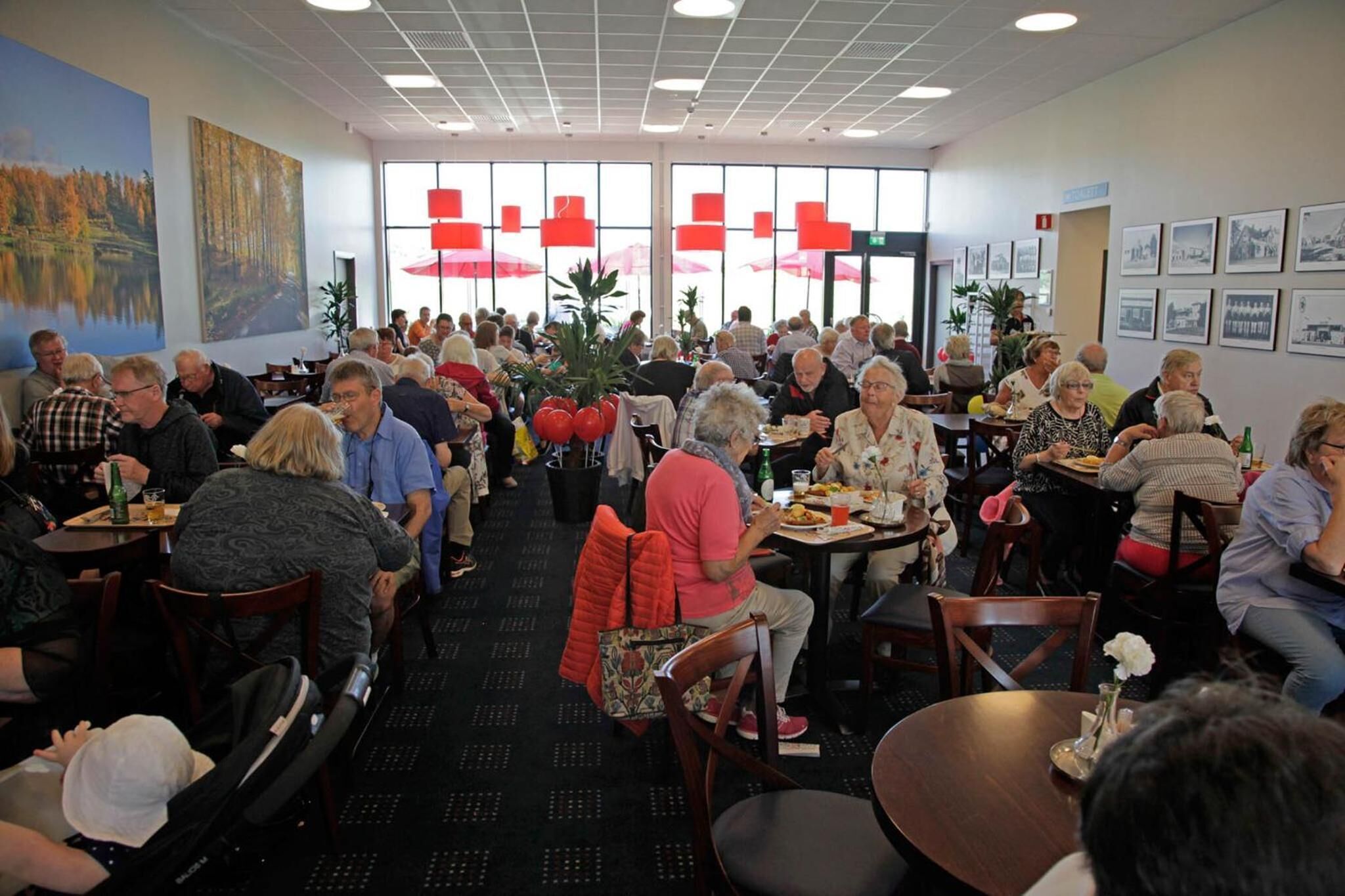A dining area with tables and chairs, large windows, and artwork on the walls.