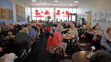 A dining area with tables and chairs, large windows, and artwork on the walls.