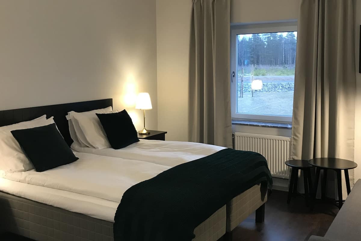 Quarto de hotel com cama, luminária de cabeceira, janela com cortinas e vista para o exterior.