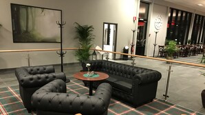 A lobby with a black leather sofa, a plaid carpet, and a large painting on the wall.