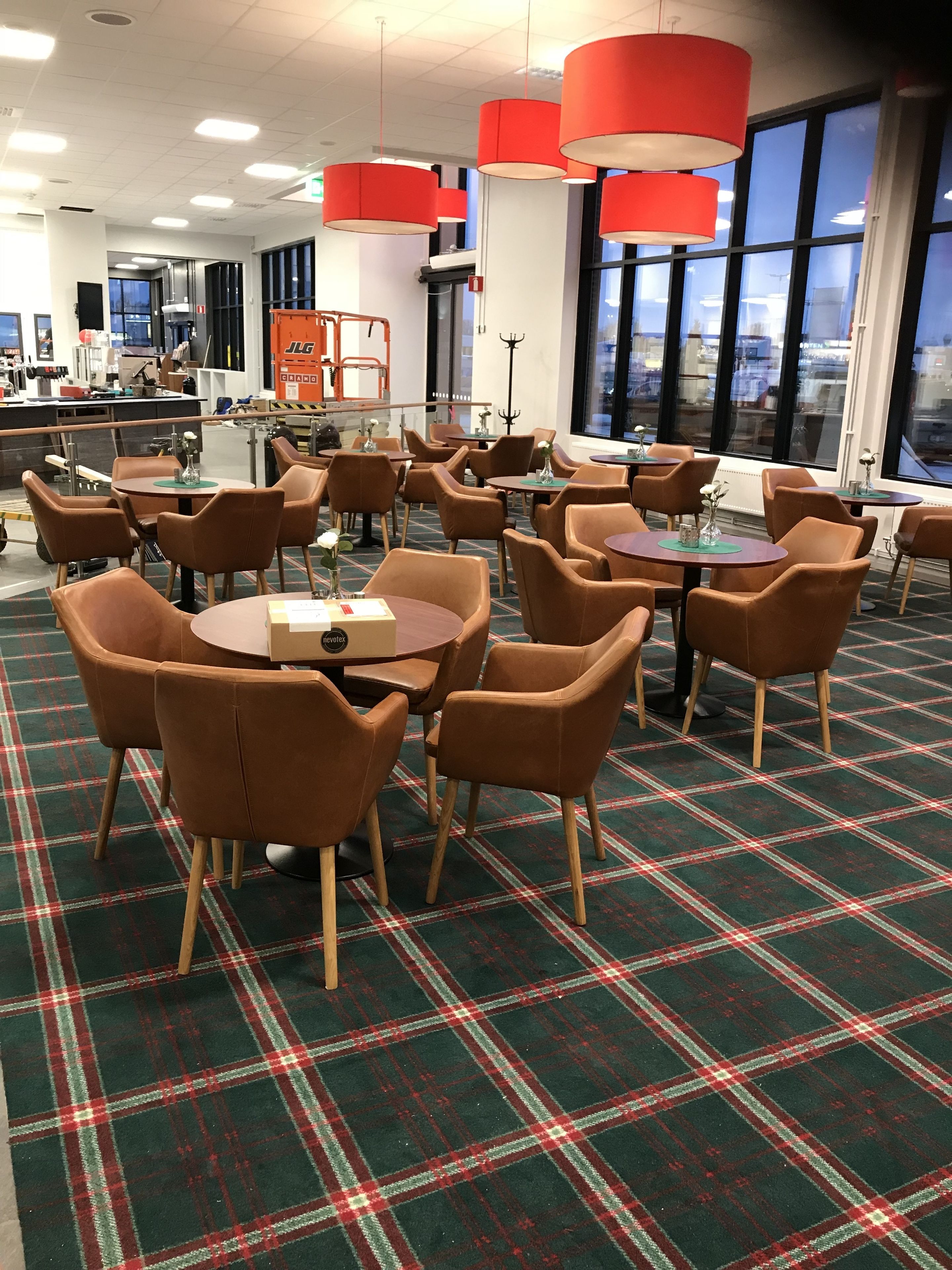 A modern dining area with round tables and brown chairs, featuring a plaid carpet and red pendant lights.