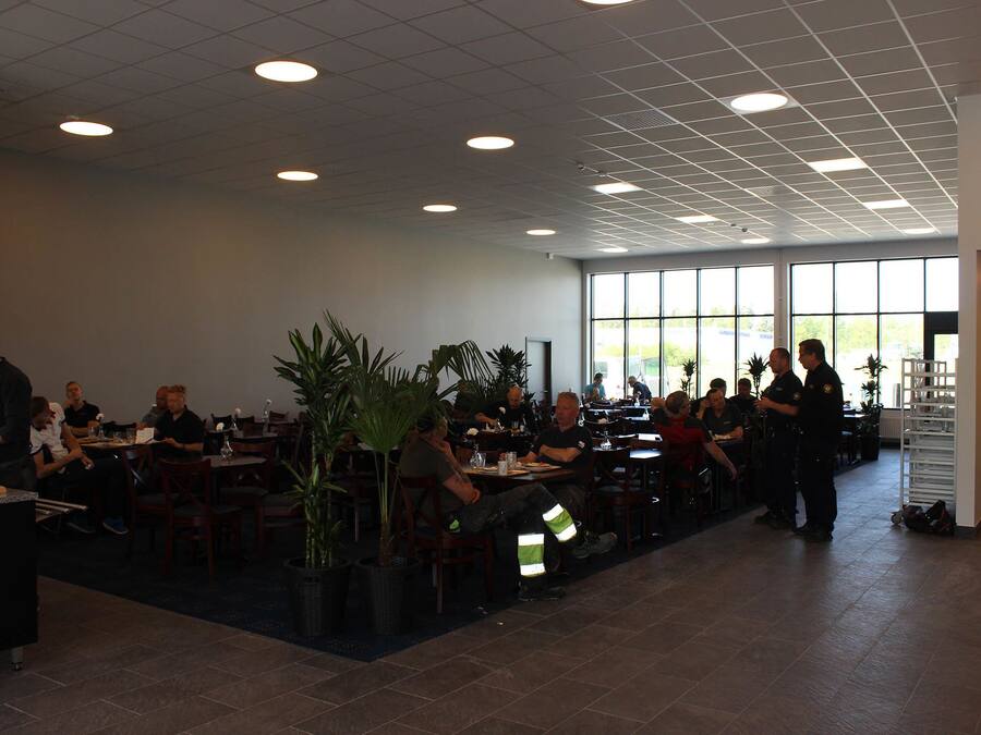 Un restaurante amplio con varias mesas y sillas, ventanas grandes y plantas en macetas.
