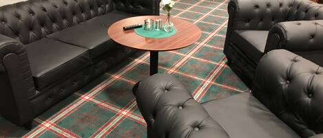 Un área de descanso moderna con alfombra escocesa, sofás de cuero y una mesa de centro redonda de madera.