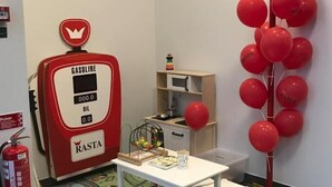 A children's play area with a toy gas pump, a table with chairs, and a balloon decoration.