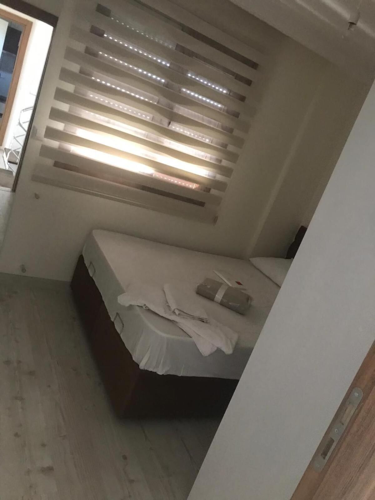 Un dormitorio con cama, ventana con persianas y suelo de madera.