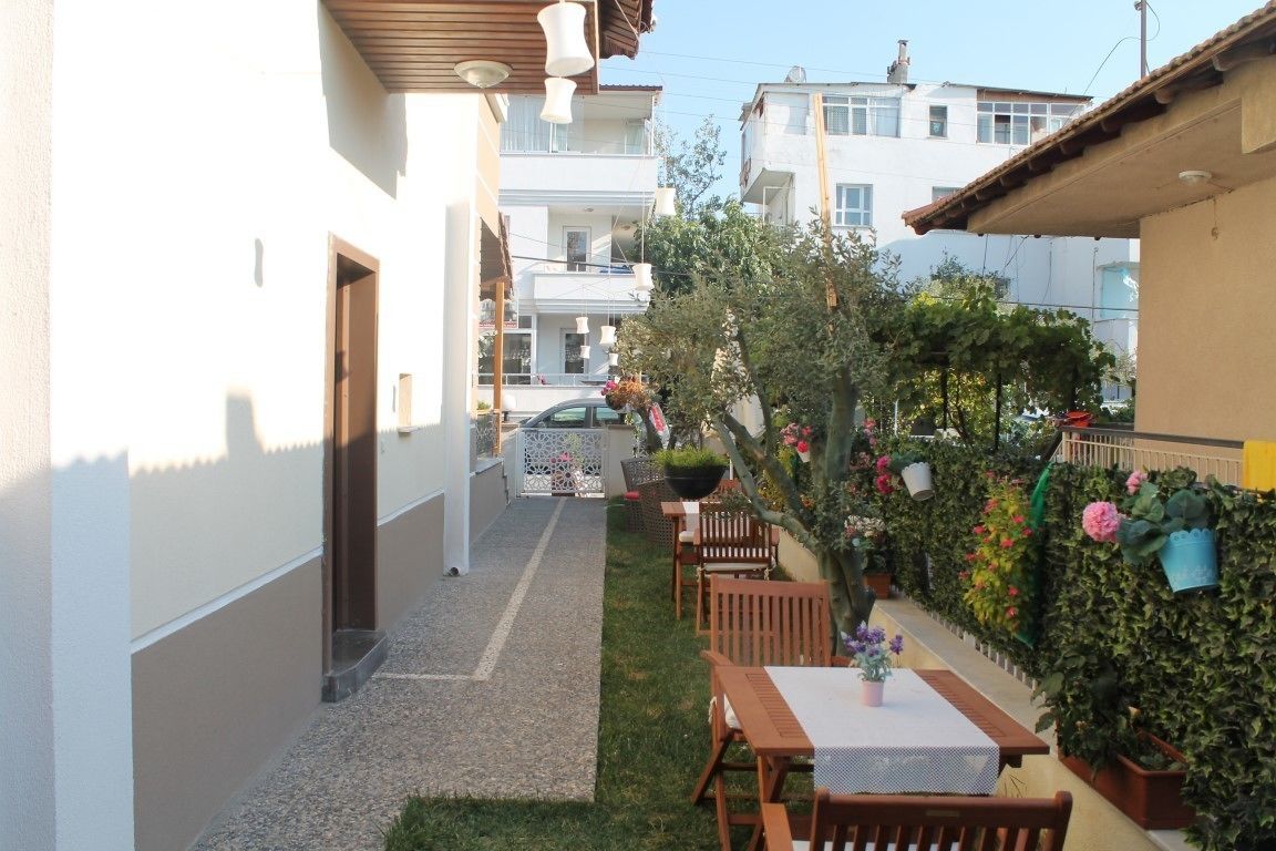 Un patio estrecho con una mesa y sillas, rodeado de follaje y una pared blanca.