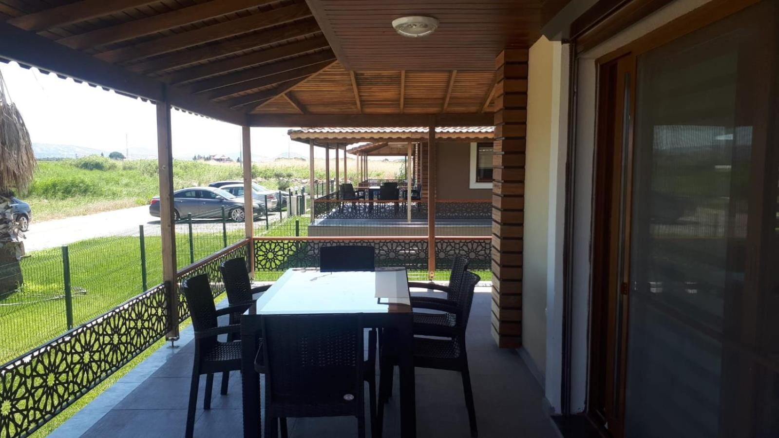 A covered outdoor patio with a table and chairs, a view of the road, and a fence.