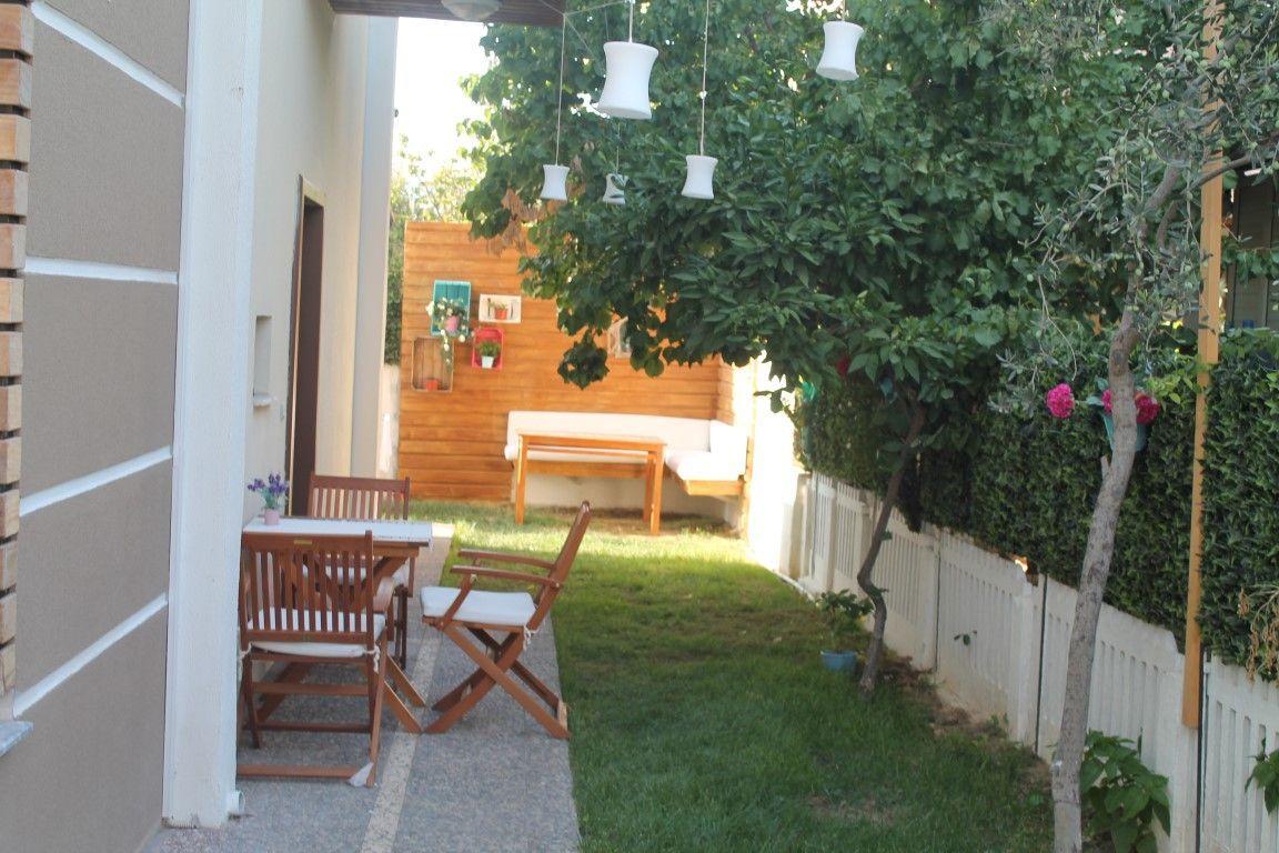 A patio with a wooden table and chairs, surrounded by a white fence and greenery.