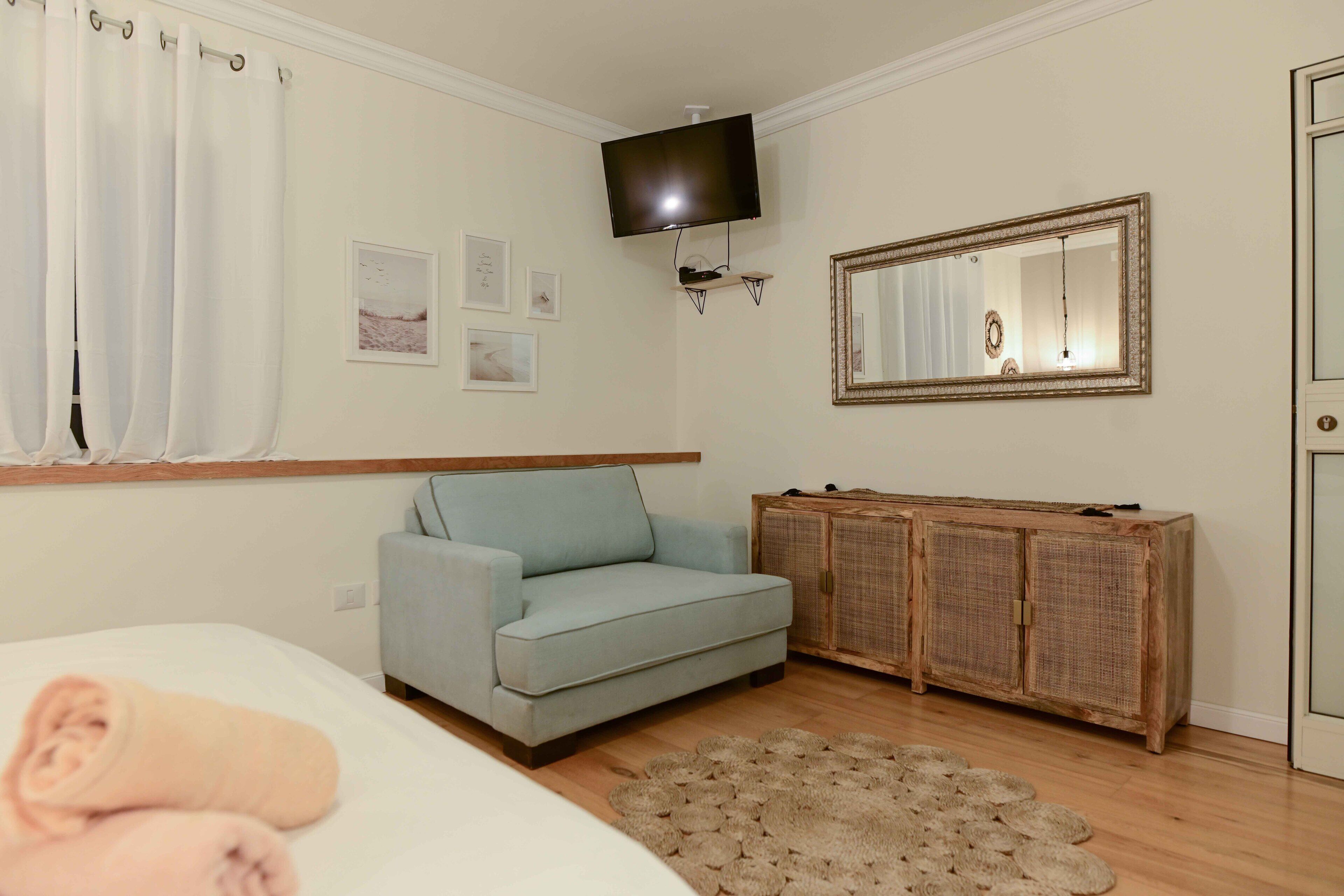 A bedroom with a light blue sofa, a wooden cabinet, a television mounted on the wall, and a mirror.