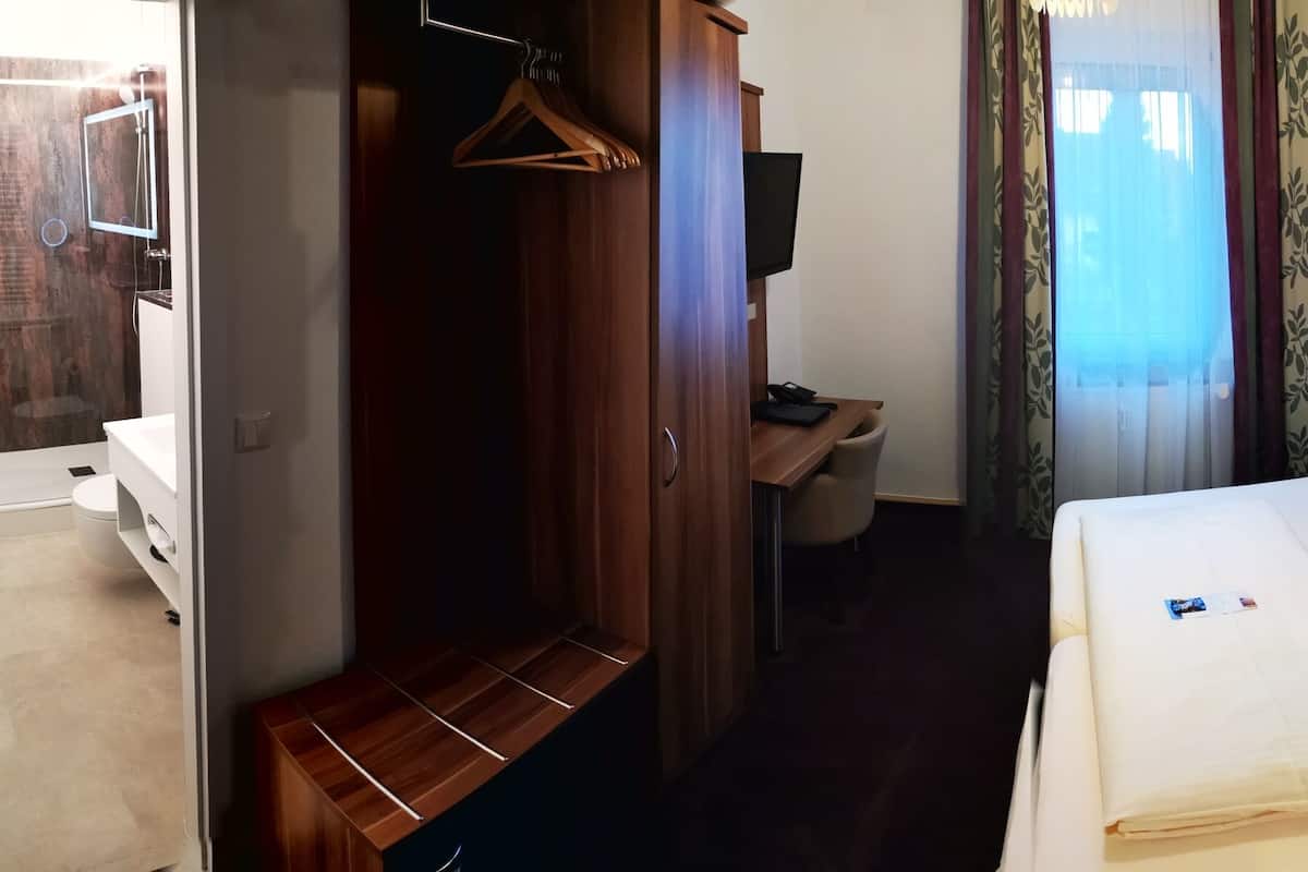 A hotel room with a bed, bedside table, and a wooden wardrobe.