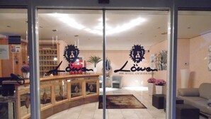 A hotel lobby with a reception desk, a seating area, and a wall with a lion logo. - Hotel Löwen (Meckenbeuren)
