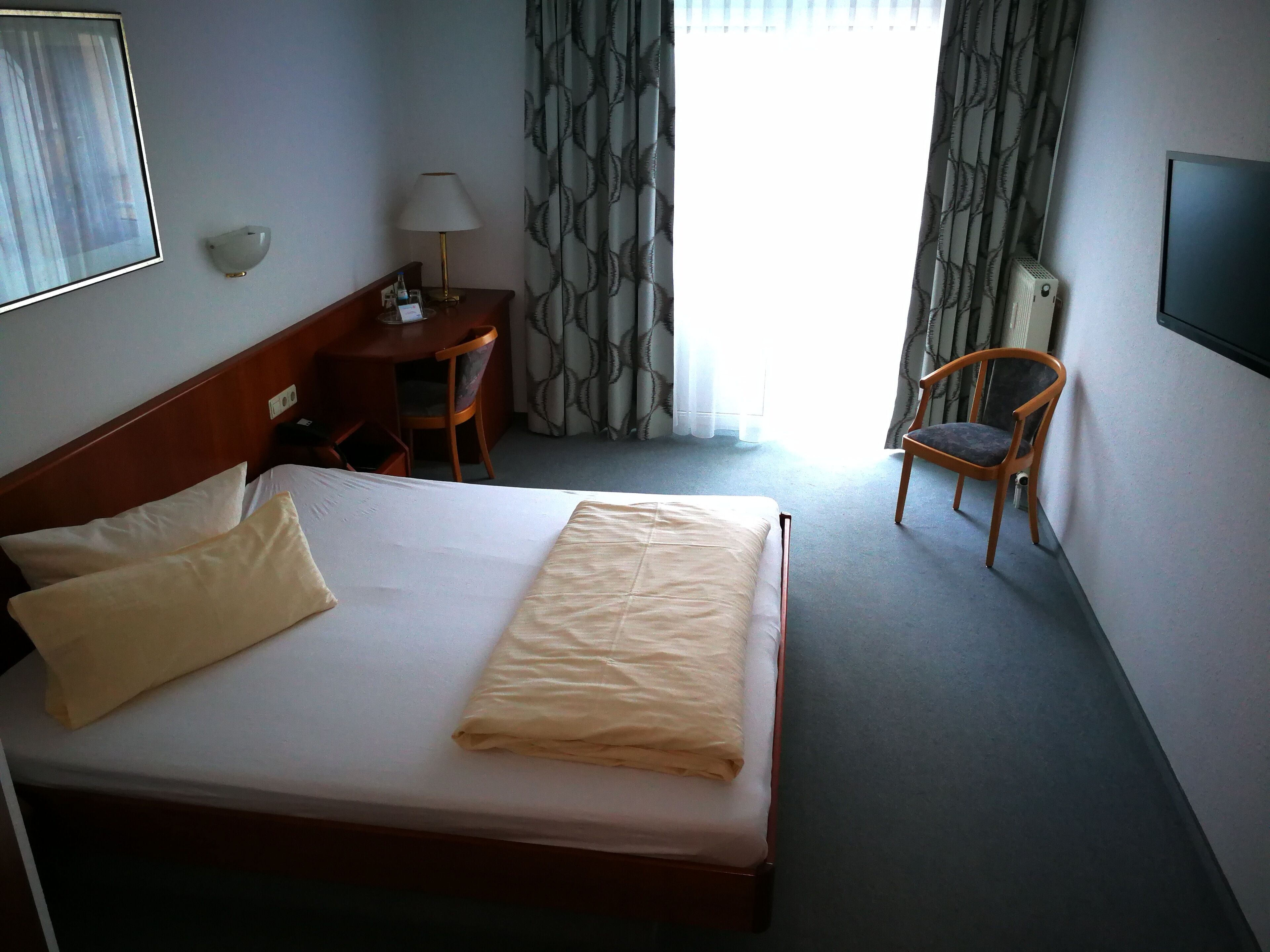 A hotel room with a bed, a desk, a chair, a TV, and a window with curtains.