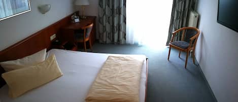 A hotel room with a bed, a desk, a chair, a TV, and a window with curtains.