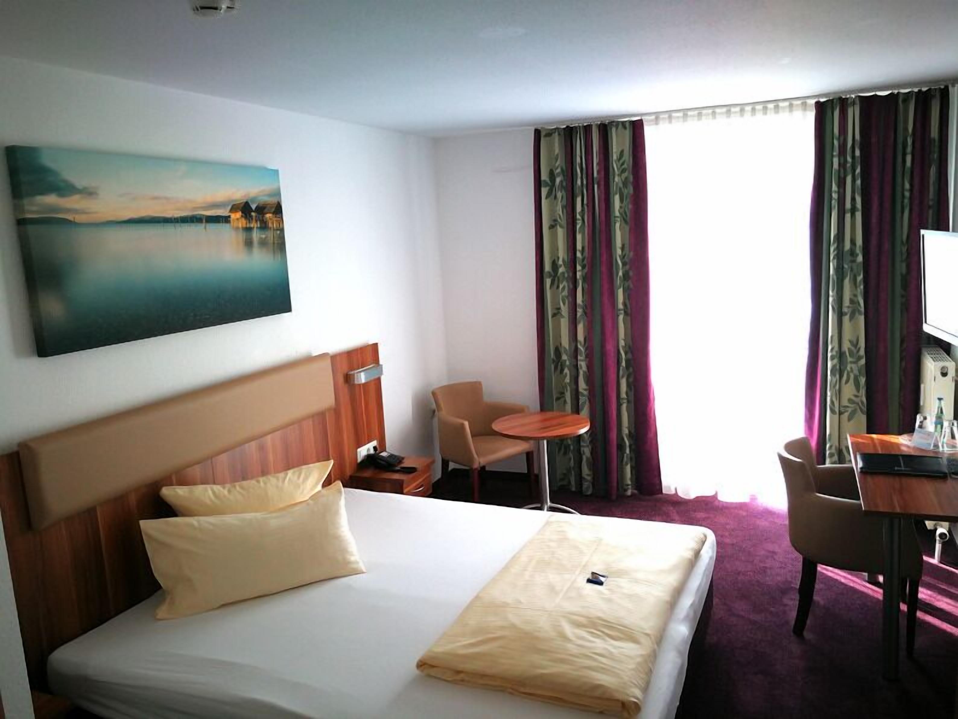 Ein Hotelzimmer mit einem Bett, einem Schreibtisch, einem Sessel, einem Fernseher und einem Bild an der Wand.