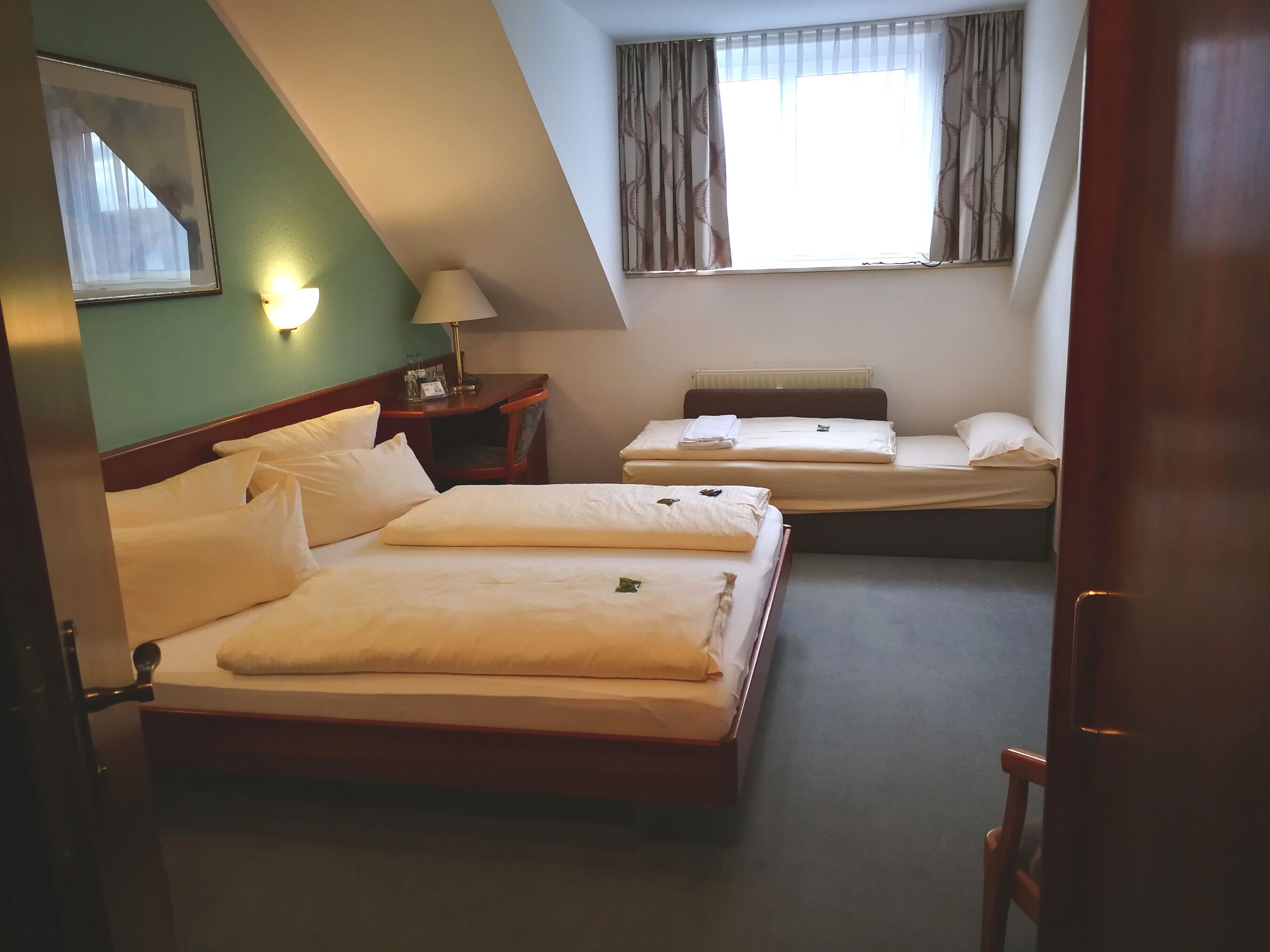 A hotel room with two beds, a nightstand, a lamp, and a window with curtains.